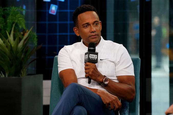 Hill Harper sitting and holding a mic